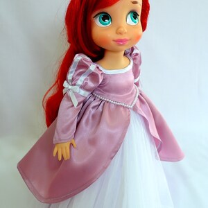 May include: A red-haired doll wearing a pink satin dress with white tulle underskirt and white satin bows on the sleeves. The doll has blue eyes and a pink blush.