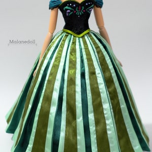 May include: A doll wearing a green and black dress with a green and white striped skirt. The dress has a black bodice with a floral design and a sweetheart neckline.