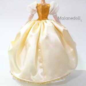 May include: A white satin ball gown with a gold bodice and white puffed sleeves. The gown has a gold trim around the bottom.