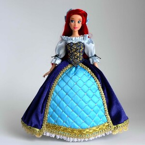 May include: A red-haired doll wearing a blue and gold dress with a white lace trim. The doll has a blue bodice with a gold and black design. The doll is wearing a blue and gold skirt with a white lace trim.