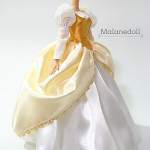 May include: A white and gold satin ball gown with a gold bodice and puffed white sleeves. The gown has a gold trim around the bottom.