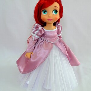 May include: A red-haired doll wearing a pink satin dress with a white tulle skirt and a pearl necklace.