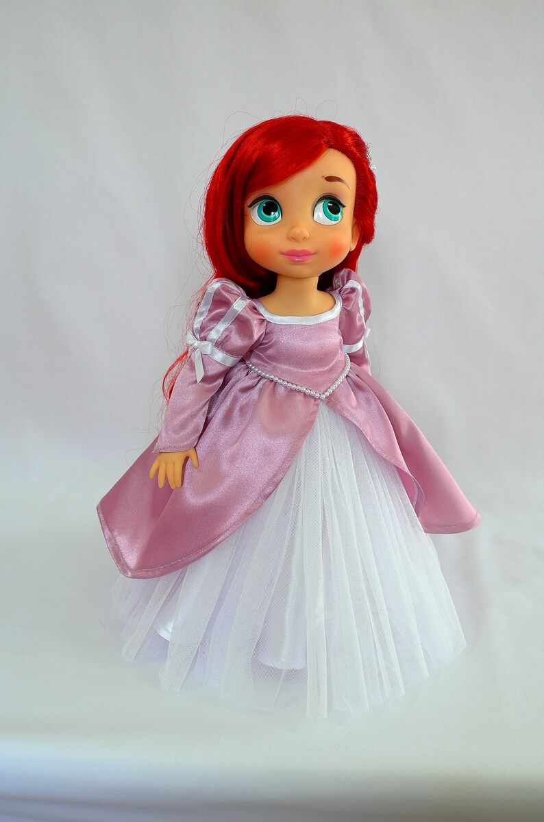 May include: A red-haired doll wearing a pink satin dress with a white tulle skirt and a pearl necklace.