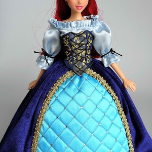 May include: A red-haired doll wearing a blue and gold dress with a blue bodice and a light blue, ruffled blouse. The doll has blue eyes and red lips.