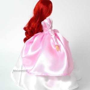 Peut inclure: Poup&eacute;e avec de longs cheveux roux et fluides, v&ecirc;tue d'une robe en satin rose avec une jupe en satin blanc. La poup&eacute;e est vue de dos, mettant en valeur le design de la robe et la texture des cheveux. C'est une poup&eacute;e de princesse.