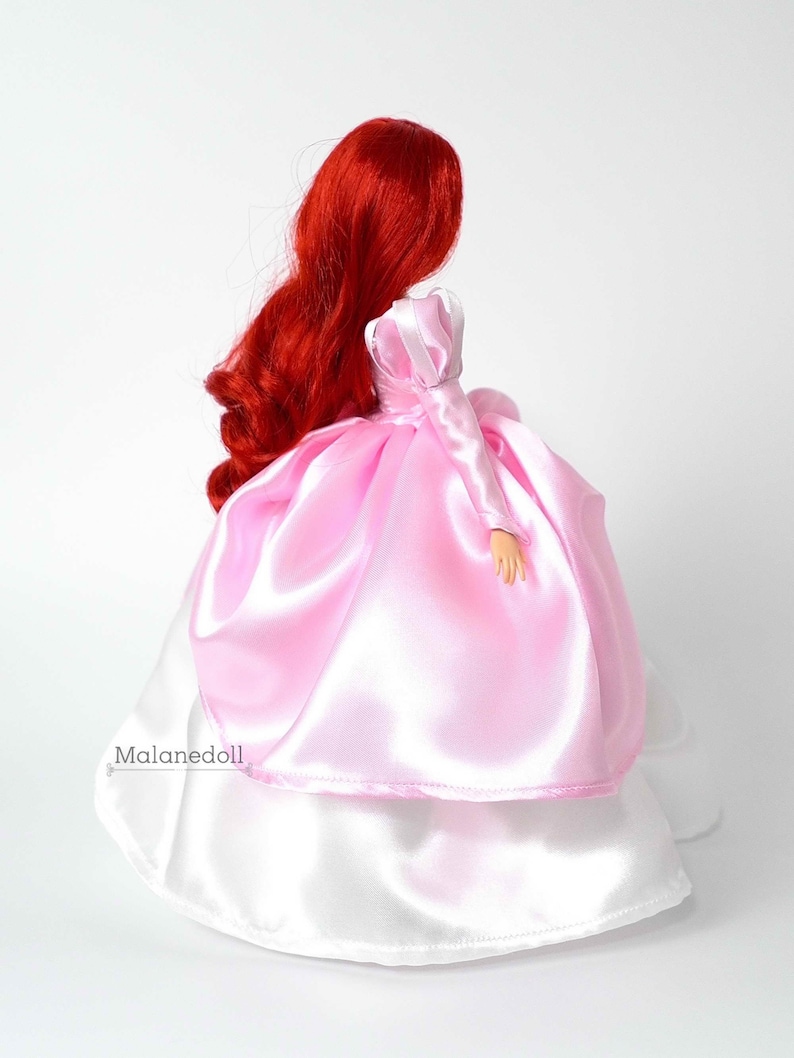 Peut inclure: Poup&eacute;e avec de longs cheveux roux et fluides, v&ecirc;tue d'une robe en satin rose avec une jupe en satin blanc. La poup&eacute;e est vue de dos, mettant en valeur le design de la robe et la texture des cheveux. C'est une poup&eacute;e de princesse.