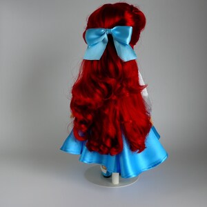 May include: A red-haired doll wearing a blue dress with a light blue bow in her hair.