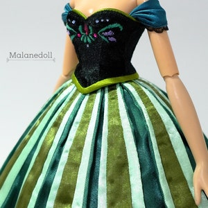May include: A doll wearing a green and white striped dress with a black bodice featuring embroidered flowers. The doll has a teal sash and a black lace trim on the shoulders.
