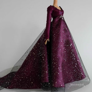 Puede incluir: Un vestido de terciopelo burdeos y tul con detalles de purpurina plateada. El vestido tiene una cola larga y un corpi&ntilde;o ajustado.