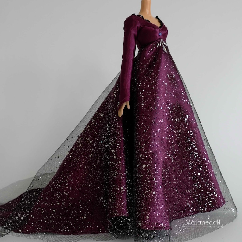 Puede incluir: Un vestido de terciopelo burdeos y tul con detalles de purpurina plateada. El vestido tiene una cola larga y un corpi&ntilde;o ajustado.