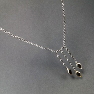 Op de afbeelding: Een zilveren ketting met drie gouden ruitvormige hangers.