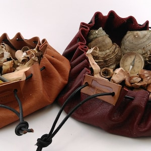 May include: Two leather pouches with drawstrings, one brown and one burgundy, filled with tinder, kindling, and a compass.