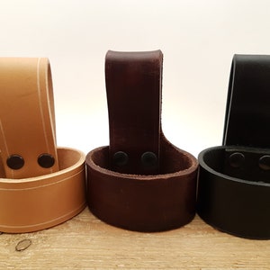 May include: Three leather cup holders in different colors: tan, brown, and black. Each holder has a loop at the top and two rivets on the side.