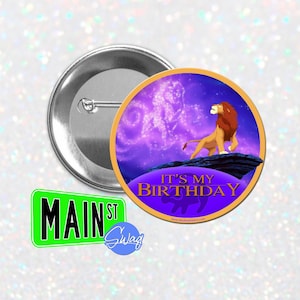 Puede incluir: Un botón con un diseño de león de dibujos animados, el texto "IT'S MY BIRTHDAY" y un letrero verde "MAIN ST". El león está sobre un fondo morado y azul. El botón es redondo y tiene una parte trasera de metal.