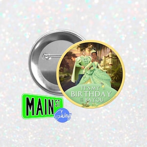 May include: A round button with a picture of a cartoon couple, a prince and a princess, walking in a green and yellow landscape. The text on the button says "It's my birthday on the Bayou".