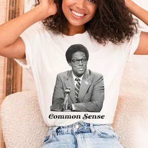 May include: White t-shirt featuring a black and white photograph of a man wearing glasses and a suit. The text "Common Sense" is printed below the image.