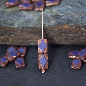 May include: Two purple and copper coloured glass beads with a diamond pattern. The beads are strung on a thin wire.