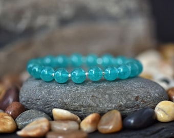 May include: A turquoise blue gemstone bracelet with silver beads. The bracelet is resting on a grey rock.