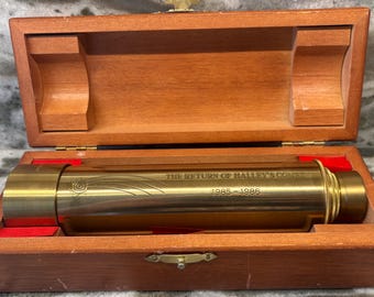 Könnte beinhalten: Ein Messing-Teleskop in einer Holzkiste. Auf dem Teleskop steht "THE RETURN OF HALLEY'S COMET 1985-1986". Die Kiste ist aus hellbraunem Holz und hat einen Messingverschluss.