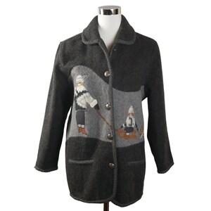 Könnte beinhalten: Eine graue Wolljacke mit einem gestickten Winterszenario auf der Vorderseite. Die Szene zeigt zwei Kinder, eines beim Skifahren und das andere beim Schlittenfahren.