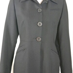 May include: A long black coat with a collar and five buttons down the front. The coat has pockets on the sides and a fitted waist.