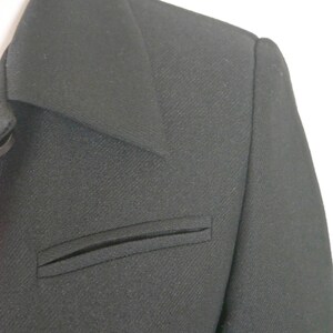 May include: A black blazer with a single flap pocket on the left side. The blazer has a notched collar and a smooth, textured fabric.