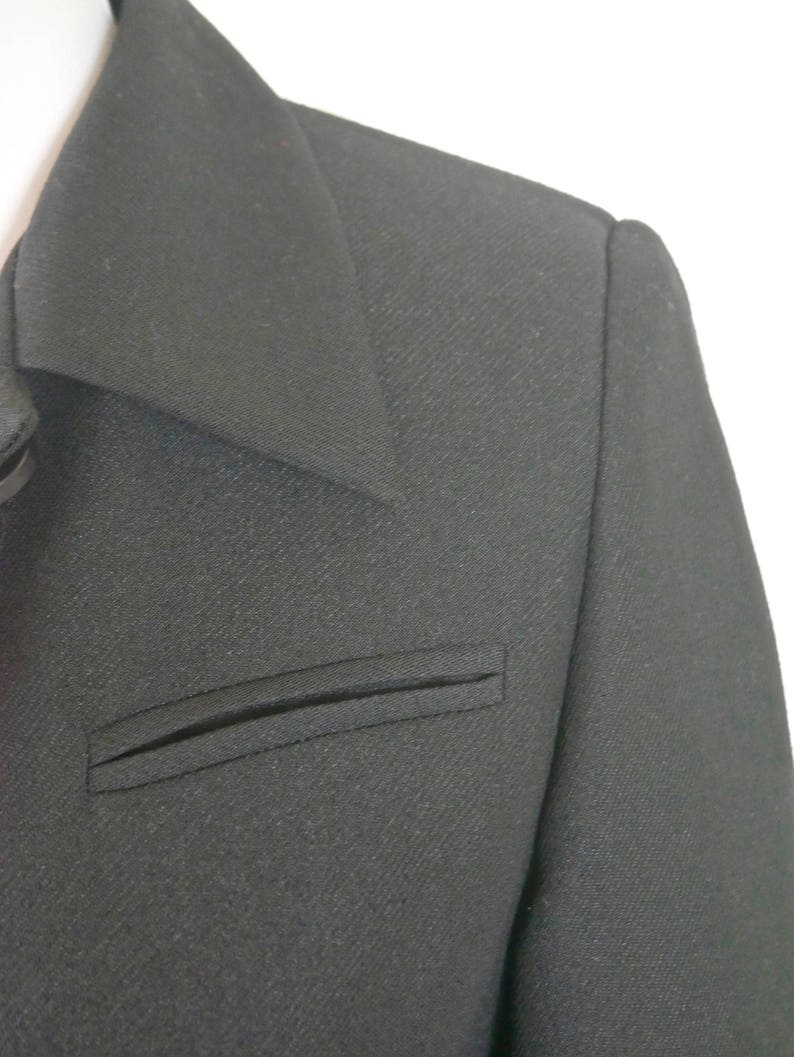May include: A black blazer with a single flap pocket on the left side. The blazer has a notched collar and a smooth, textured fabric.