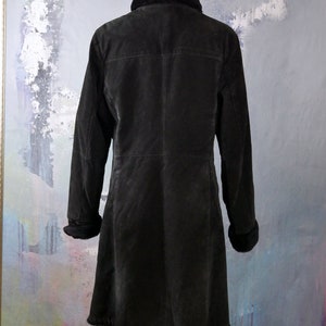 May include: A long black suede coat with a faux fur collar and cuffs. The coat has a button closure and a straight silhouette.