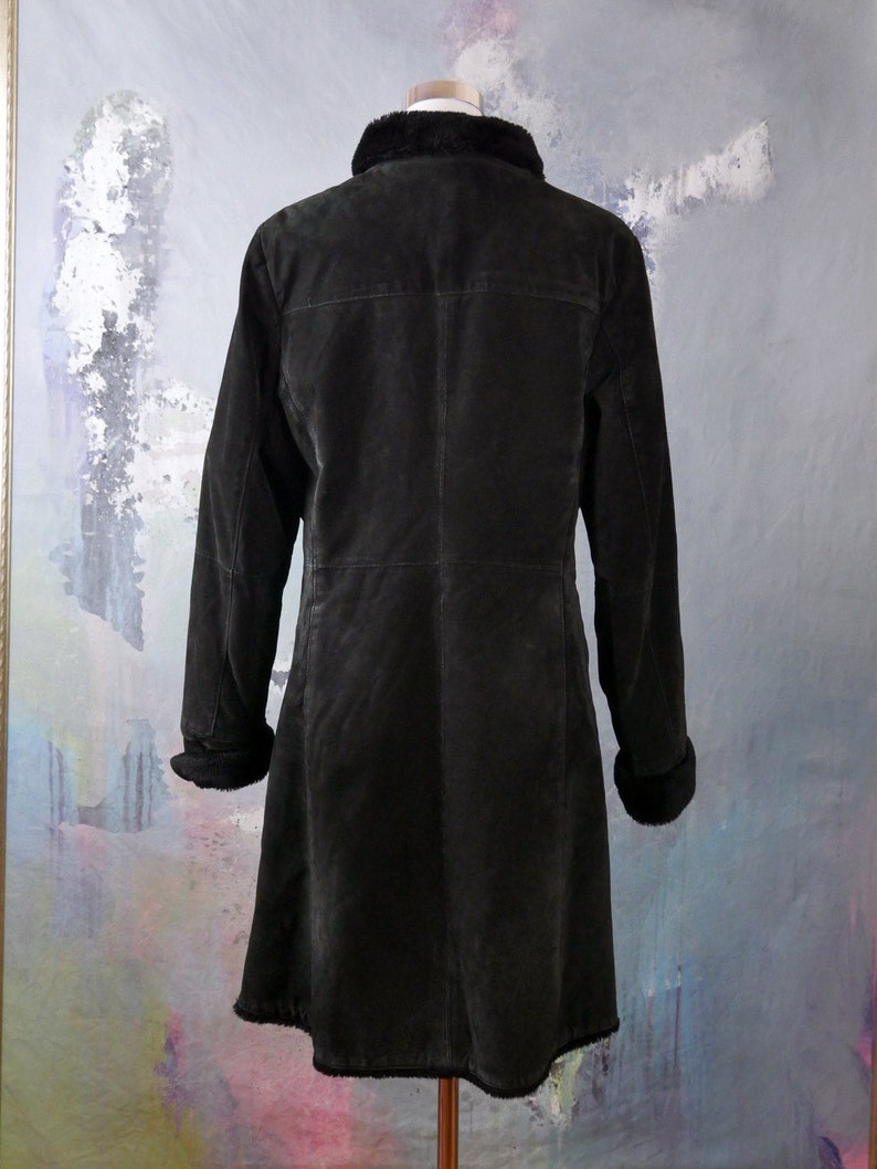 May include: A long black suede coat with a faux fur collar and cuffs. The coat has a button closure and a straight silhouette.