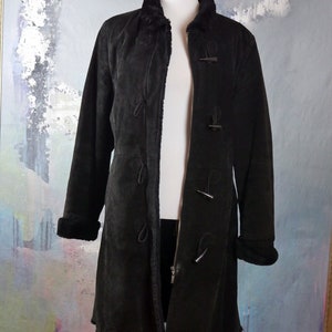 May include: A long black suede coat with a fur collar and toggle closures. The coat has a zipper closure and is lined with a soft, fuzzy material.