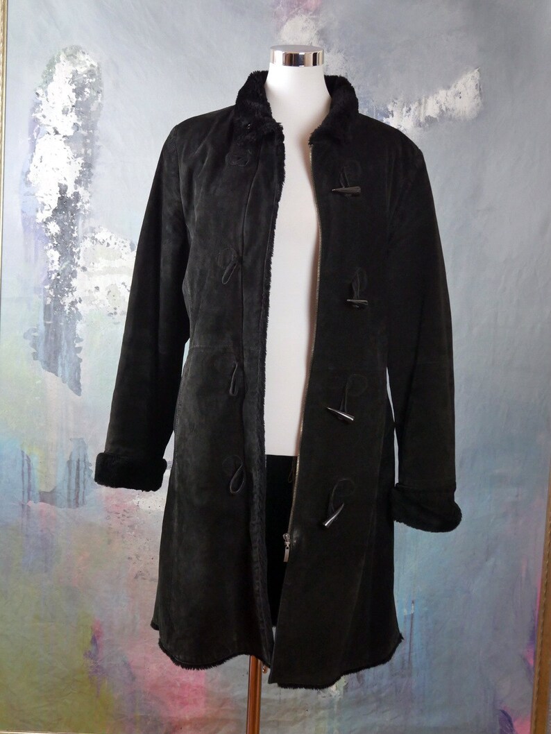 May include: A long black suede coat with a fur collar and toggle closures. The coat has a zipper closure and is lined with a soft, fuzzy material.