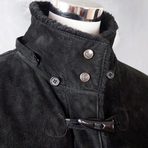 May include: Black suede jacket with a fur-lined collar and a toggle closure. The jacket has a buttoned placket and two pockets.
