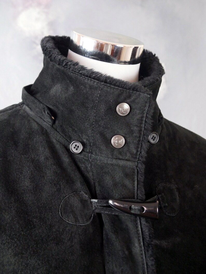 May include: Black suede jacket with a fur-lined collar and a toggle closure. The jacket has a buttoned placket and two pockets.