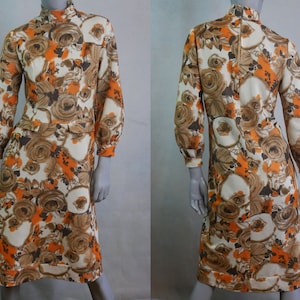 Puede incluir: Un vestido de manga larga con cuello alto y estampado floral en tonos naranja, marrón y blanco. El vestido tiene un corpiño ajustado y una falda ligeramente acampanada.