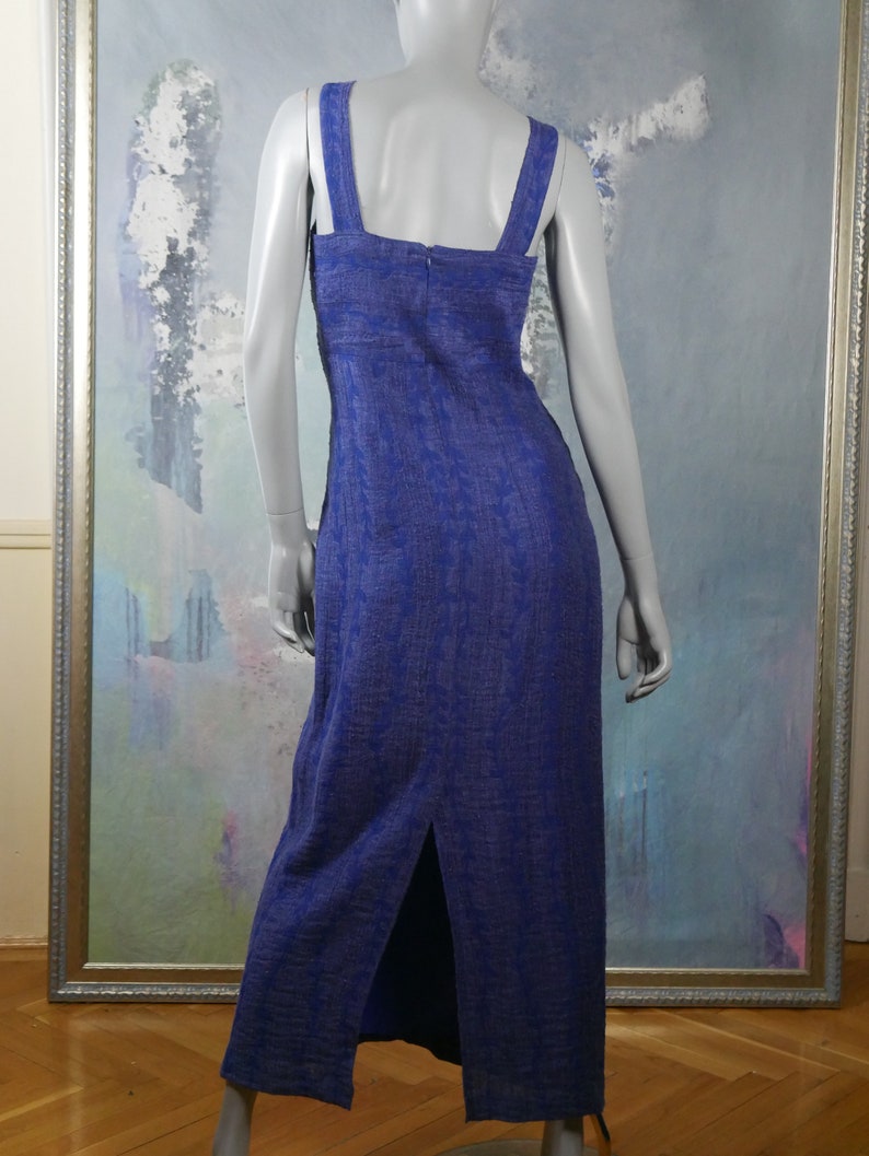 May include: A long, sleeveless, blue dress with a white pattern. The dress has a square neckline and a slit up the back.