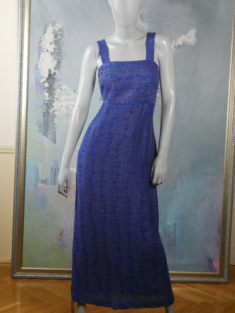 May include: A long, blue, sleeveless dress with a square neckline and a subtle pattern. The dress is made of a lightweight fabric and has a relaxed fit.