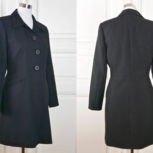 May include: A black long-sleeved coat with a collar and three buttons down the front. The coat has a fitted waist and a straight skirt.
