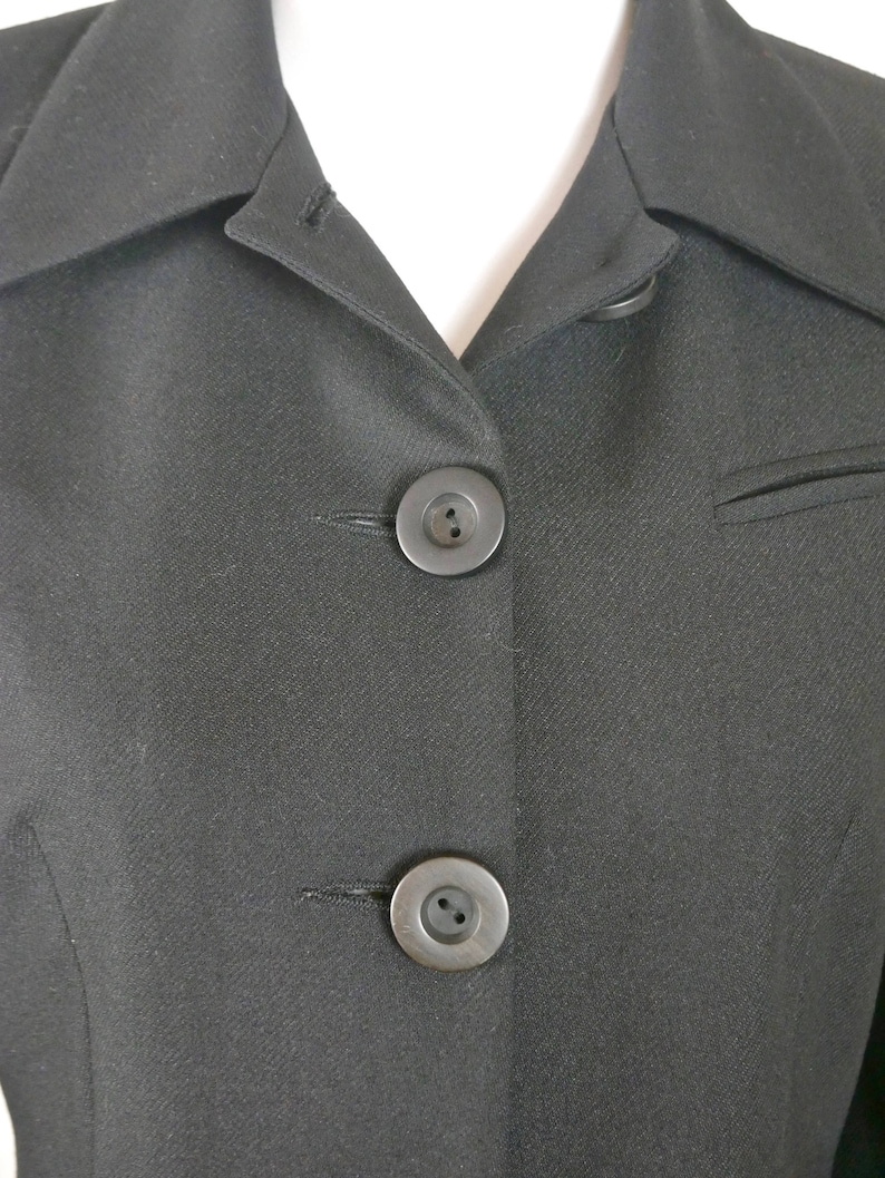 May include: Close-up of a black blazer with two black buttons. The blazer has a classic, tailored look.