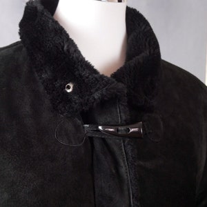 May include: A black suede jacket with a faux fur collar and a black toggle closure.