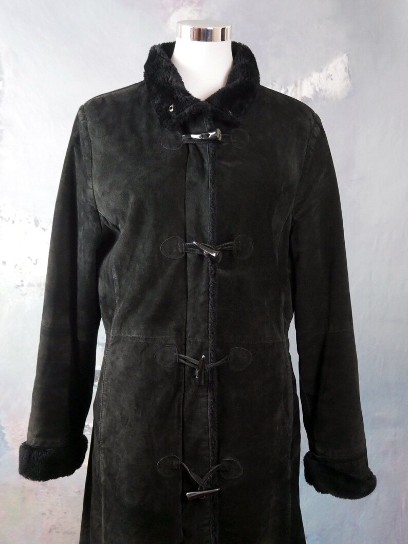 May include: A long black suede coat with a faux fur collar and cuffs. The coat has a toggle closure and is lined with a soft fabric.