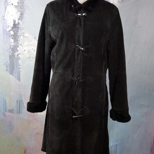 May include: A black suede coat with a faux fur collar and cuffs. The coat has a long, fitted silhouette and features a button closure with toggle accents.
