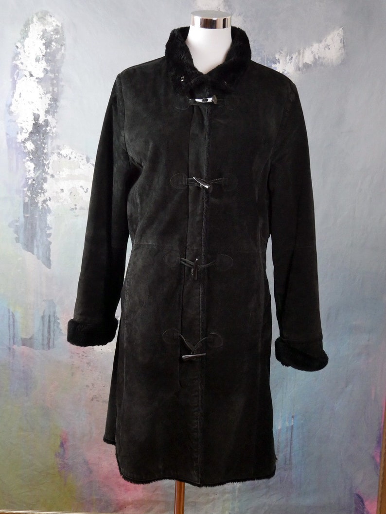 May include: A black suede coat with a faux fur collar and cuffs. The coat has a long, fitted silhouette and features a button closure with toggle accents.