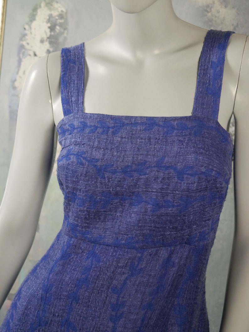 May include: A sleeveless dress with a square neckline and a blue and white floral pattern. The dress is made of a textured fabric and has a fitted bodice and a flowing skirt.