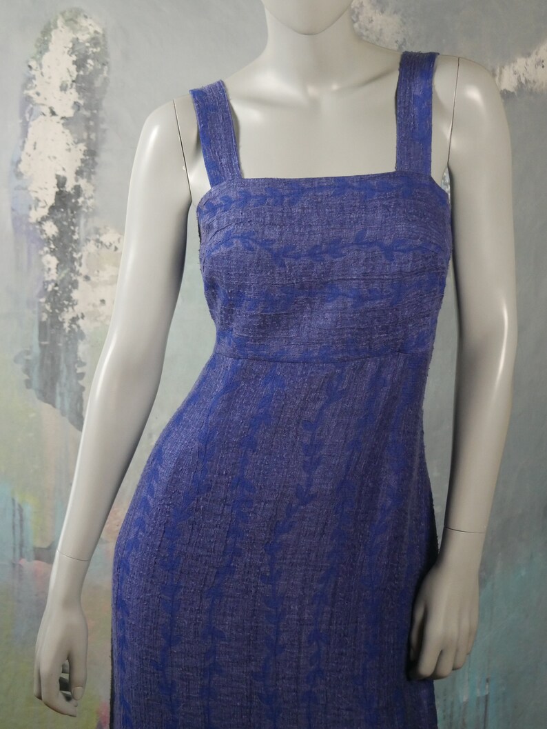 May include: A long, sleeveless dress with a square neckline and a floral pattern. The dress is made of a textured fabric and is a deep blue color.