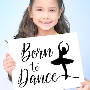 May include: A white sign with the words "Born to Dance" in a cursive font, accompanied by a black silhouette of a ballerina. The sign is held by a smiling child against a light blue background.