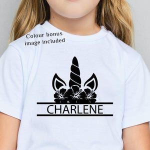 Pode incluir: Camiseta branca com um desenho de unicórnio preto, incluindo um chifre, orelhas e detalhes florais. O nome "CHARLENE" é impresso em preto abaixo do gráfico do unicórnio. O texto "Colour bonus image included" também é visível.