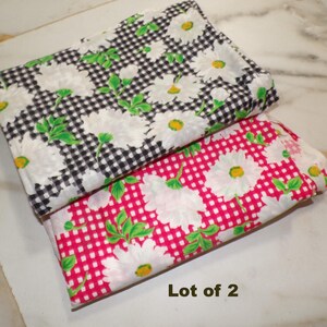 May include: Two folded fabric pieces. One features a black and white checkered pattern with white daisy flowers and green leaves. The other has a pink checkered pattern with white daisy flowers and green leaves. The text "Lot of 2" is visible.
