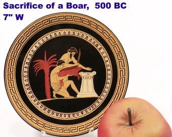 May include: A Greek plate with a black background and a decorative border. The plate features a scene of the Sacrifice of a Boar, 500 BC. The plate is 7 inches wide. An apple is in the foreground.