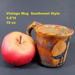May include: A vintage Southwest style mug with a textured, glazed finish in shades of brown, orange, and green. The mug features a black graphic and a handle with a decorative element. It is 3.5 inches high and holds 10 ounces.