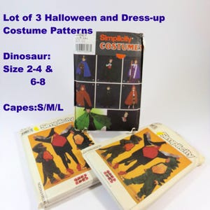 May include: Three Simplicity costume pattern packets. The main packet features various cape designs. Two additional packets show dinosaur costumes. Text on the packets includes "Dinosaur: Size 2-4 & 6-8" and "Capes: S/M/L".